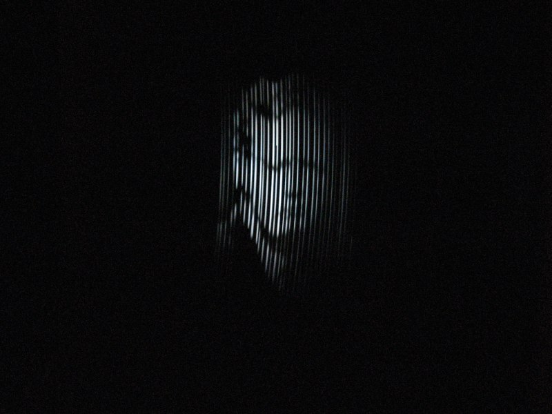 Figure 7 — A working NBTV disc televisor's "first light" moment: a recognisable face, scanned through the disc's spiral of apertures, visible as a series of narrow illuminated strips rather than a smooth cont…